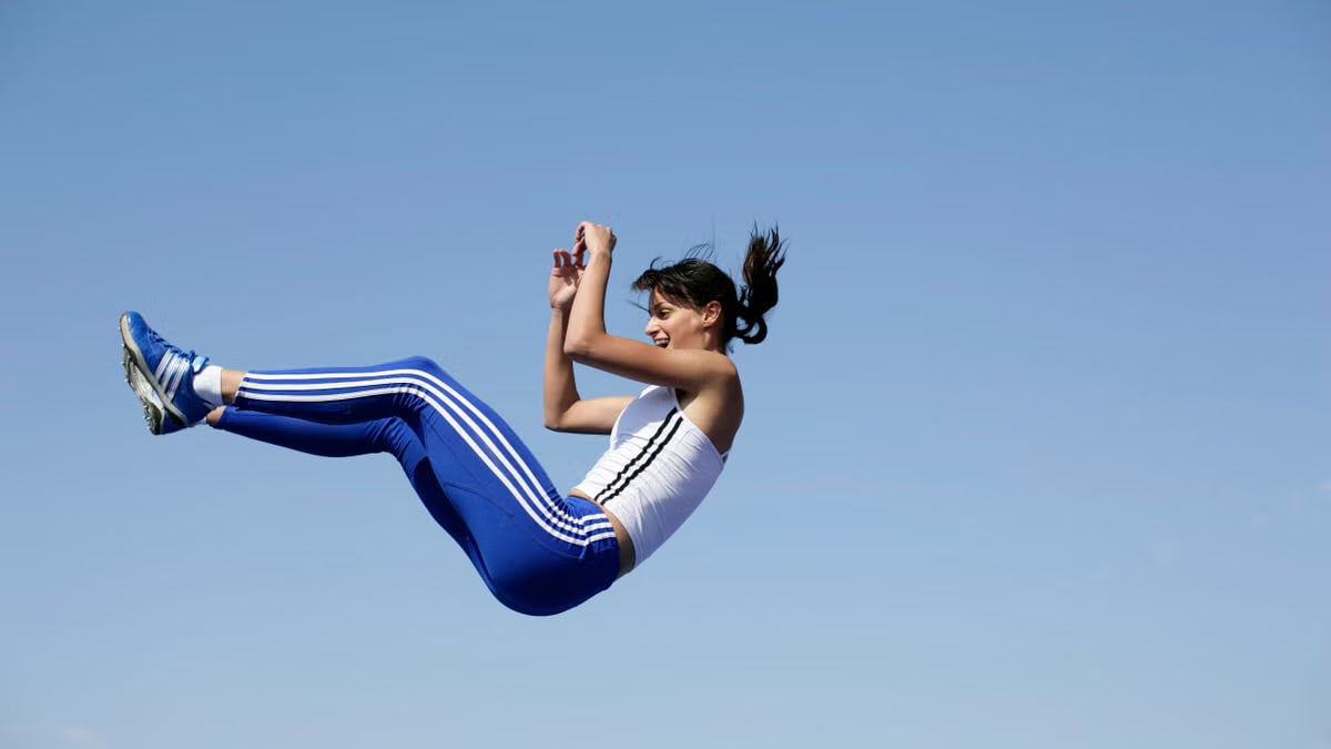 A woman in blue sportswear jumps energetically against a clear sky.